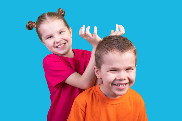 kleines Mädchen setzt einem Jungen auf blauem Hintergrund Hörner auf - Foto, Bild
