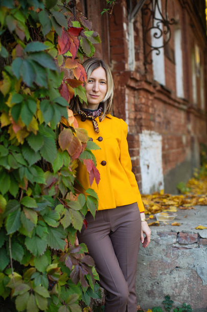 Kobieta w żółtej kurtce pozuje na jesiennej ulicy z żółtymi liśćmi. - Zdjęcie, obraz