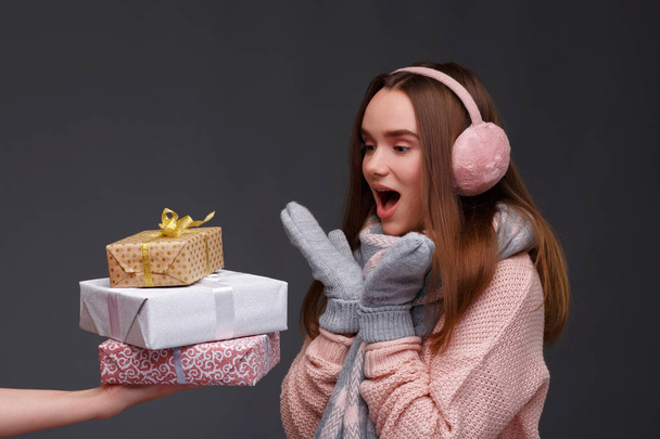 Happy excited young beautiful smiling girl in knitting pullover and pink fluffy earmuffs with gift boxes. Xmas model with long straight hair. Winter holidays, Christmas, New Year concept.  - Fotoğraf, Görsel