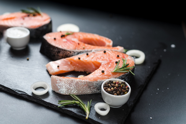 raw salmon steak on a dark stone background with onions, rosemary, spices, concept diet, unsaturated fats, omega 3 - Photo, Image