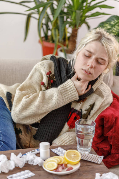 Дівчинка в светрі хвора лежить на дивані. Застуда і грип. Пацієнт застудився, відчуваючи хворобливість і біль у горлі. Нездорова дівчина з болем в горлі
. - Фото, зображення