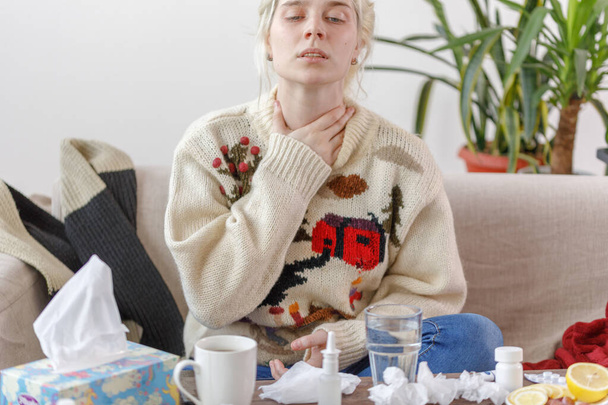 Дівчинка в светрі хвора, сидить на дивані. Застуда і грип. Пацієнт застудився, відчуваючи хворобливість і біль у горлі. Нездорова дівчина з болем в горлі
. - Фото, зображення