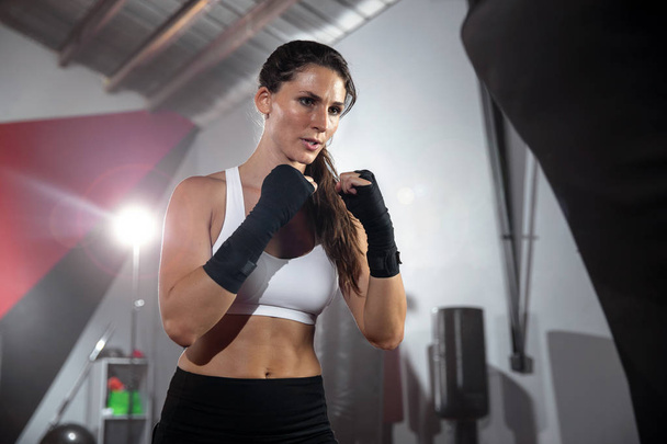 Akcja styl życia portret pięknej kobiety sportowiec ćwiczenia i szkolenia w siłowni, spocony, trzymając pięści do góry gotowy do ataku worka bokserskiego - Zdjęcie, obraz