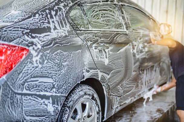 Автомойка, рабочие используют пену для чистки серых автомобилей до пены по всему автомобилю. Перед использованием воды высокого давления для смывания
 - Фото, изображение