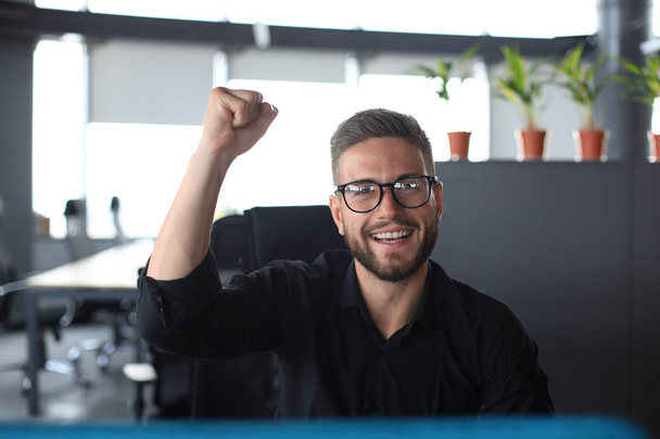 Handsome businessman is keeping arm raised and expressing joyful in office - Foto, Imagen