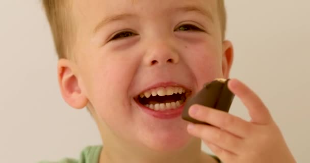 Vidám gyermek nevet és csokoládét eszik a kezében - Felvétel, videó