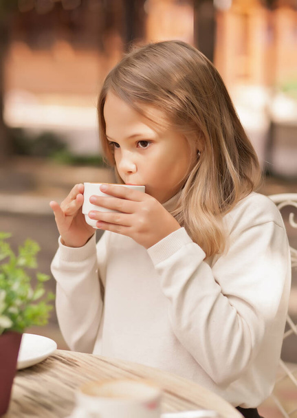 Pretty little girl smiling and drinking cappuccino in outdoor cafe - Foto, Bild
