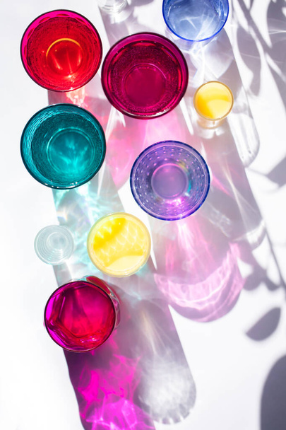 Glass goblets create wonderful coloured shadows on a solar table. The shadow of sunlight reflect to glass of pink and yellow, emerald colors. Top view. - Φωτογραφία, εικόνα