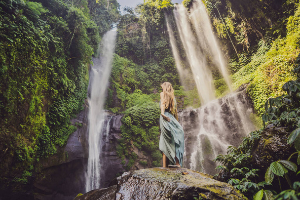 Woman in turquoise dress at the Sekumpul waterfalls in jungles on Bali island, Indonesia. Bali Travel Concept - Фото, изображение