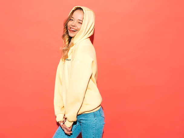 Portret van jong mooi lachend meisje in trendy hippe hippe gele hoodie.zorgeloze vrouw poseren in de buurt van roze muur in de studio. Positief model hebben plezier - Foto, afbeelding