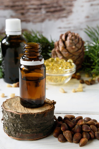 композиция кедрового масла с кедровыми орехами на фоне ветки с сосновым конусом, на светлом деревянном фоне
 - Фото, изображение