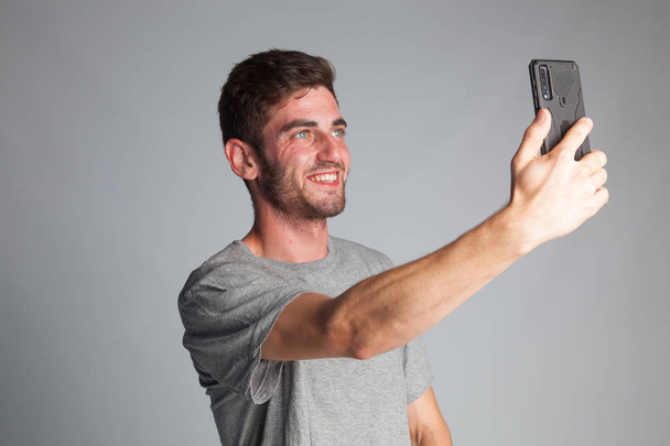 Jonge jongen maakt een selfie met zijn smartphone, trekt gezichten en uitdrukkingen - Foto, afbeelding