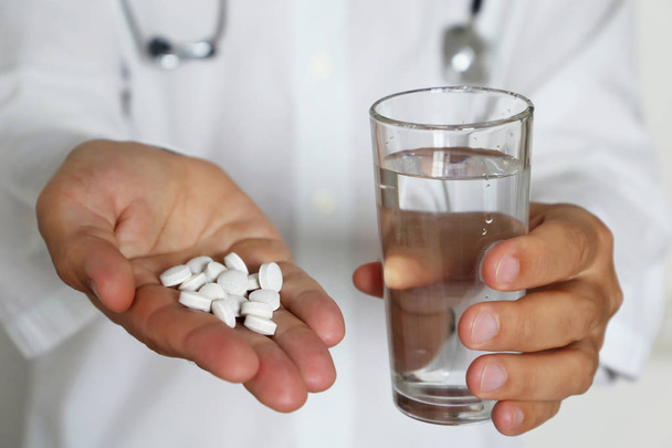 Az orvos tablettákat és egy pohár vizet ad, az orvos a tenyerében tartja a gyógyszert fehér tablettákban. A gyógyszer, az orvosi vizsgálat, a gyógyszerész, az antibiotikum vagy a vitaminok adagjának fogalma - Fotó, kép