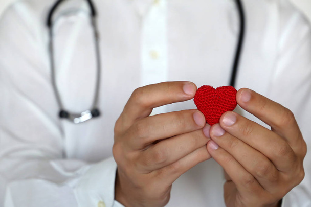 Kardiológia és egészségügy, orvos piros kötött szívet tart a mellkas közelében. A kardiológus koncepciója, véradás, szívbetegség kezelése a klinikán, sztetoszkópos diagnózis - Fotó, kép