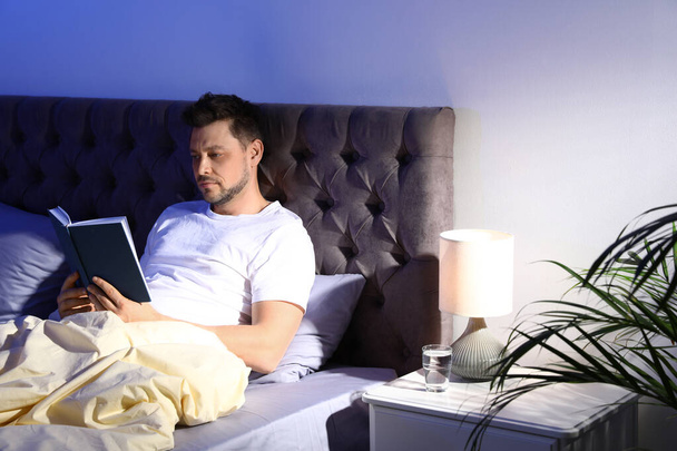 Handsome man reading book in dark room at night. Bedtime - Zdjęcie, obraz