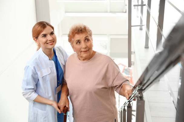 Enfermeira assistindo a mulher idosa em escadas dentro de casa
 - Foto, Imagem