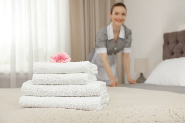 Stack of clean towels on bed and blurred chambermaid in hotel room, closeup. Space for text - Фото, изображение