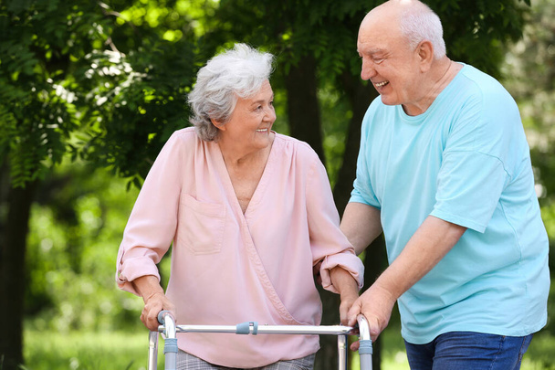 Elderly man helping his wife with walking frame outdoors - Photo, image