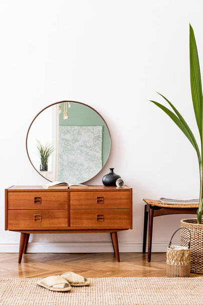 Stylish and modern interior of living room with elegant accessories. Round mirror and wooden commode - 写真・画像