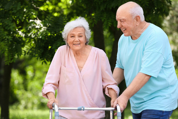 Oudere man helpt zijn vrouw met wandelen frame buitenshuis - Foto, afbeelding