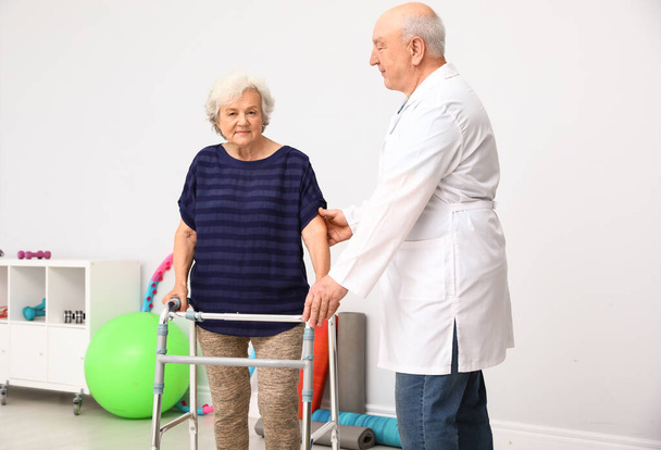 Doctor helping elderly woman with walking frame indoors - Foto, Imagen