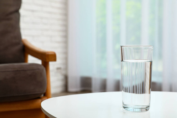 Glass of water on table in room, space for text. Refreshing drink - Foto, Bild