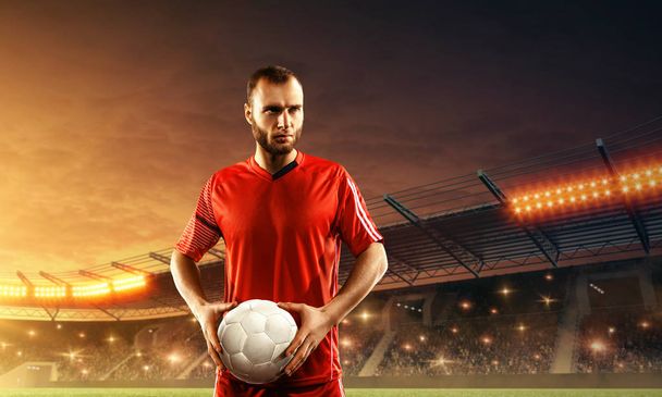 Jonge professionele voetballer in sportuniform met een bal. Voetbalwedstrijd in een stadion. Fans juichen.  - Foto, afbeelding