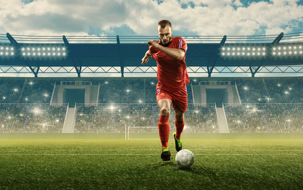 Fiatal profi focista sport egyenruhában, akcióban egy labdával. Focimeccs egy stadionban. Rajongók éljeneznek. Felhőkék ég - Fotó, kép