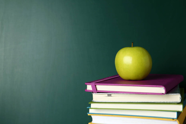 Books and apple near green chalkboard, space for text. School education - Zdjęcie, obraz