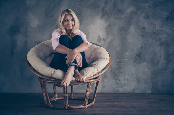 Full length photo of peaceful quite middle aged wear pastel color jumper denim jeans dream about her future holidays have break pause sit in wicker armchair in living room indoors - Fotoğraf, Görsel