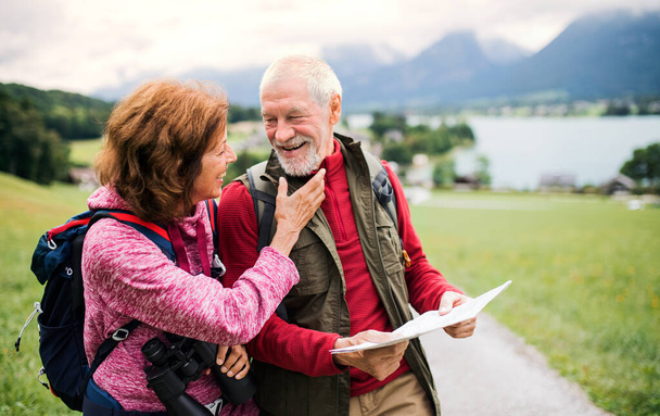 Senior pensioner couple with hiking in nature, using binoculars and map. - Fotó, kép