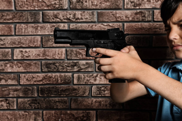 Little child playing with gun against brick wall. Dangerous game - Photo, image