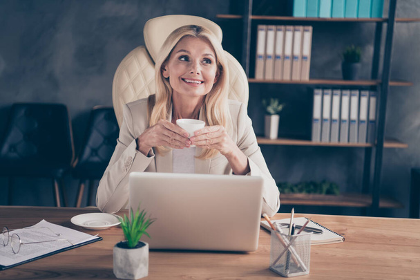 Photo of cheerful positive ceo holding cup of tea with hands sitting in front of computer having relax with glasses taken off - Фото, зображення