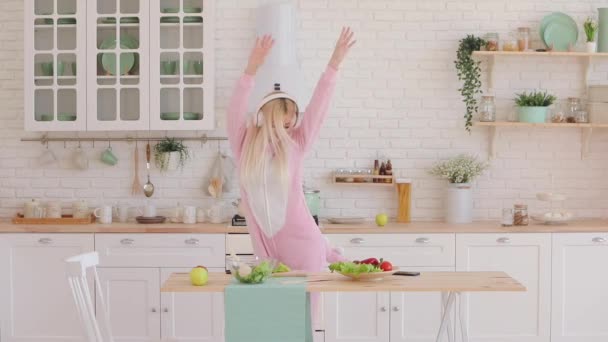 blonde haired girl in kigurumi listens to music in kitchen - Video