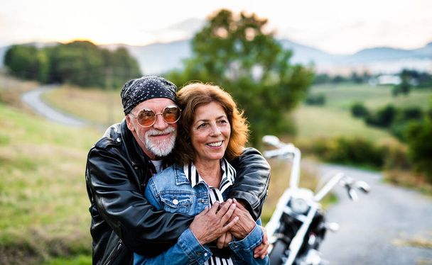A cheerful senior couple travellers with motorbike in countryside. - Фото, зображення