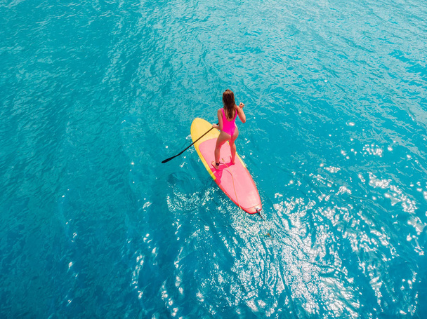 Atractiva mujer en stand up paddle board en un tranquilo océano azul
. - Foto, imagen