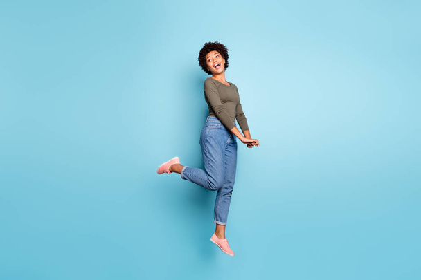 Full length body size photo of cheerful cute charming nice jumping black millennial girlfriend excited with compliment wearing jeans denim green sweater isolated over blue vivid color background - Foto, imagen