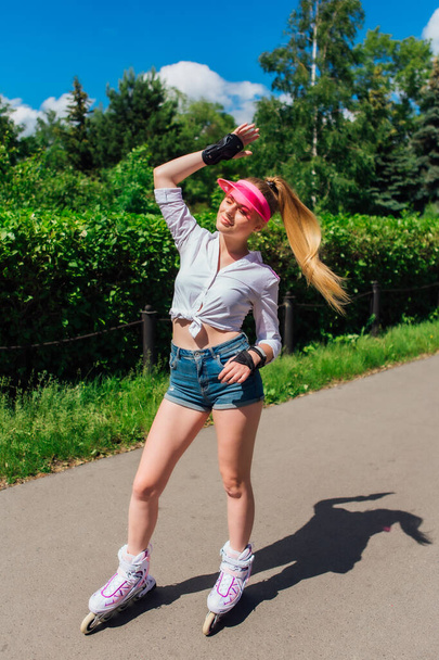 Portrait of an emotional girl in a pink cap visor and protective gloves for rollerblades and skateboarding riding on rollerblades on the road. - Foto, immagini