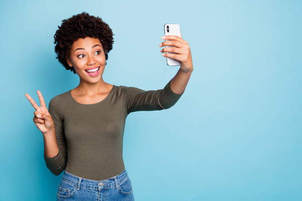 Copyspace photo of cute nice charming fascinating black woman kind friendly showing v-sign to those she speaks with video call wearing jeans denim greed sweater isolated vivid blue color background - Foto, afbeelding