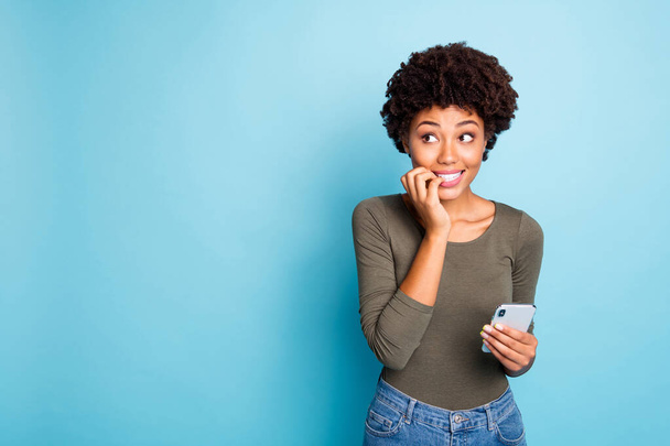 Portrait of scared emotions expression mulatto girl use cellphone have social media trouble failure send sms by mistake panic nail bite look wear green trendy pullover isolated blue color background - Foto, imagen