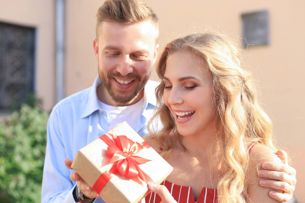 Astonished excited couple in summer clothes smiling and holding present box together while standing on city street - Fotoğraf, Görsel