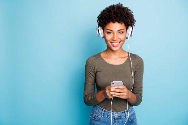 Copyspace photo of cheerful cute charming nice toothy girlfriend black skinned holding her phone with hands looking at you wearing jeans denim green sweater isolated over blue vivid color background - Fotó, kép