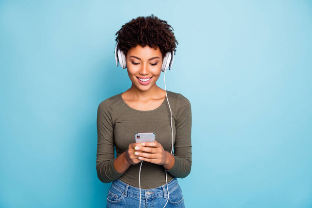Photo of cheerful cute nice attractive trendy black girlfriend searching for new songs through her phone as answering people on social media isolated over blue vivid color background - Foto, Imagen