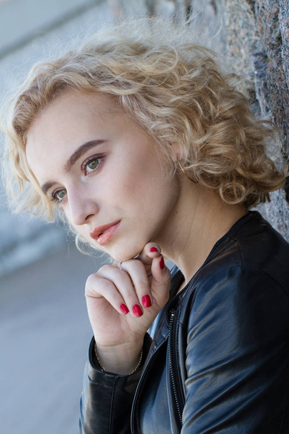 Portrait of a young blonde with bright makeup on a granite wall background - 写真・画像