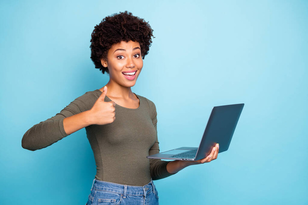 Portrait of funky funny afro american girl entrepreneur hold her laptop show thumb up recommend good sales promo discounts wear green stylish trendy sweater denim jeans isolated blue color background - Foto, Bild
