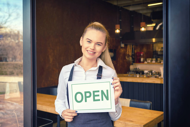Portré boldog kisvállalkozás tulajdonosa áll étterem bejáratánál - mosolygós üzletasszony részt vesz az új ügyfelek kávézóban - vidám pincérnő látható nyílt jel - Fotó, kép