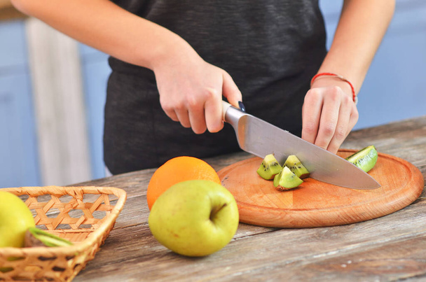 Cropped view of girl cutting tasty kiwi on chopping board - Foto, afbeelding