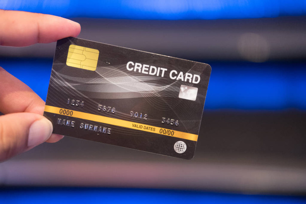 Joven sosteniendo una tarjeta de crédito en un fondo borroso de color claro
. - Foto, imagen