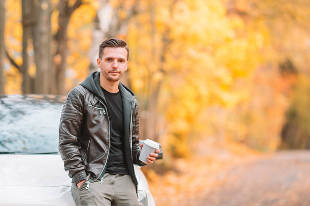 Young man drinking coffee with phone in autumn park outdoors - Fotó, kép
