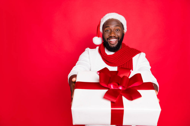 Portrait of positive brown hair afro american man in santa claus cap feel festive enjoy xmas christmas celebration tradition give big gift box wear white sweater scarf isolated over red color - Zdjęcie, obraz